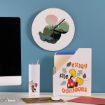 A desk with a computer, tumbler, and file holder featuring Disney’s Minnie Mouse, with a round wall clock above, all against a blue wall.
