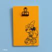 An orange wooden plaque with a black clip at the top and a black line drawing of Minnie Mouse dressed as a witch, holding a pumpkin. The Disney logo is in the bottom left corner. The background is light blue.