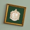 A framed Slytherin house crest from Harry Potter, featuring a silver serpent on a green background with ornate gold trim, hanging on a pale green wall.