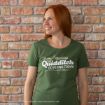 A smiling woman with long red hair wears a green "Quidditch Go Flying Today!" T-shirt and stands against a brick wall.