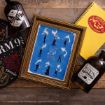 A framed blue Harry Potter art print with Patronus silhouettes sits on a wooden surface, surrounded by potion bottles, a black mat, and a yellow Hogwarts-themed notebook.