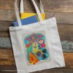 A white tote bag with a colorful Honeydukes candy shop design sits on a wooden surface. Yellow and blue notebooks peek out from the bag.