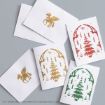 Five white cards with gold, red, and green holiday designs featuring a winged beast and a decorated tree, laid out on a gray background.
