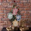 A small Christmas tree decorated with Harry Potter house crests ornaments and green and red baubles, with wrapped gifts underneath, set against a brick wall.