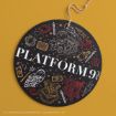 A round black ornament with "PLATFORM 9¾" in white text, illustrated with a train, owl, books, trolley, and magical items, and a rope for hanging. Harry Potter designs are in gold, white, and red.