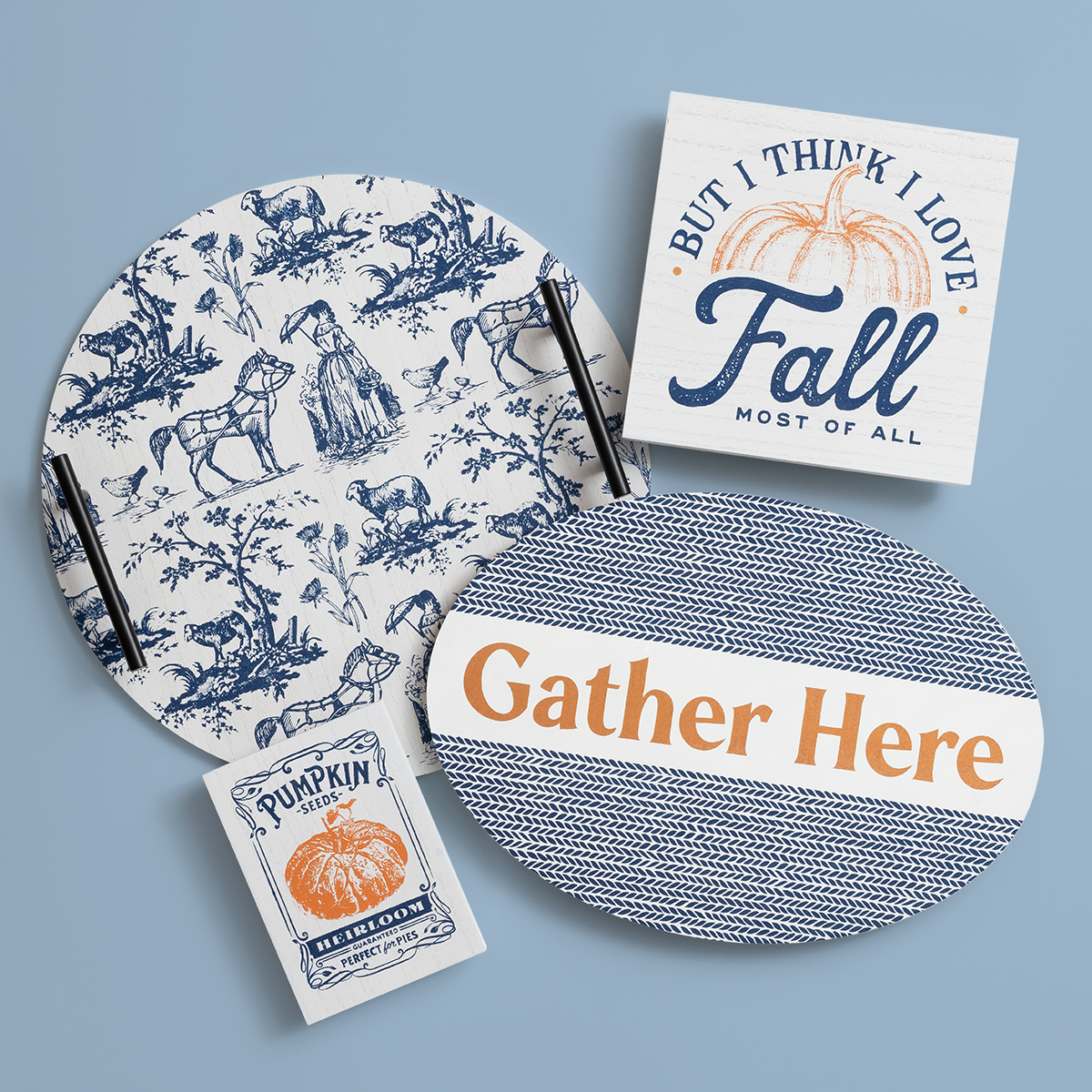 Four fall-themed decor pieces on a light blue background: a round toile tray, a “Gather Here” oval sign, a “Fall Most of All” pumpkin sign, and a “Pumpkin Time” matchbox.