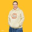 A smiling person wearing a light yellow hoodie with “Sweater Weather” and cartoon characters printed on it, standing against a solid yellow background.