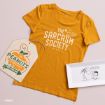 Flat lay of a mustard yellow “The Sarcasm Society” t-shirt, a Peanuts-themed pumpkin patch sign, and a rectangular plate with a Peanuts comic illustration featuring Snoopy and Lucy.