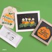 Four Peanuts-themed items: a pumpkin patch tag, a framed art of characters with pumpkins, a wooden sign reading “It’s The Great Pumpkin Charlie Brown,” and a tray with Snoopy laughing, all on a green background.