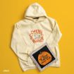 A cream hoodie with “Sweater Weather” and Peanuts characters printed on it, next to a framed artwork of a pumpkin labeled “It’s The Great Pumpkin, Charlie Brown,” on a yellow background.