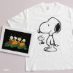 A white T-shirt with Snoopy and Woodstock printed on it is next to framed Peanuts art with Charlie Brown, Snoopy, and friends behind pumpkins under a starry sky.