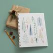 A spiral sketchbook with hand-drawn colorful trees, a wrapped gift with pine and twine, a pencil, and small pinecones on a green background.