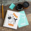 A notebook with a Halloween Winnie the Pooh design, a pencil, mint-green eraser, black chalk paste, and two stencils are on a rustic wooden table. The notebook reads “BOO? POOH!” with Pooh and Piglet in costumes.