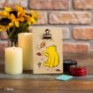 A wooden card with Winnie the Pooh catching autumn leaves is clipped upright on a wooden table, next to candles, a small tin, a blue square, and sunflowers, with a brick wall in the background.