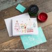 A Winnie the Pooh holiday card with “Merry Everything” text sits on a rustic table with a turquoise stencil, red paste, and an envelope. Pooh holds gifts, and the card is decorated with trees, stars, and festive accents.