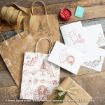 Gift bags, cards, and wrapping paper featuring red and brown line drawings of Winnie the Pooh characters are arranged on a wooden surface with twine, pine sprigs, and a wrapped present.