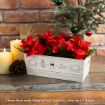 A white box decorated with Winnie the Pooh drawings holds red flowers and greenery. It’s placed on a wooden table near lit candles and a small Christmas tree with ornaments.