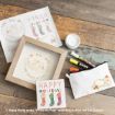 Assorted holiday-themed Winnie the Pooh crafts and art supplies, including greeting cards, a framed print, markers, and a pencil case with Pooh illustration, arranged on a wooden surface.