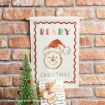 A wall hanging with “BEARY CHRISTMAS” and a drawing of Winnie the Pooh in a Santa hat. In front, there’s a small Christmas tree and a wrapped gift. Brick wall background.