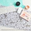 A desktop with a Winnie the Pooh-themed mat, keyboard, mouse, teal stencil, black jar, peach paint dish, and a pink sign reading “Warm & Cosy” with a mug, marshmallows, and holly.