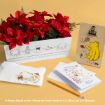 White box with red poinsettias, Winnie the Pooh-themed pouch, a pencil, greeting cards, and a gift bag featuring Pooh and autumn leaves, all arranged on a yellow surface.