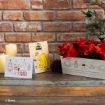 A holiday scene with Winnie the Pooh-themed cards, red flowers in a festive box, a mini Christmas tree, pinecone, and lit candles, set against a brick wall.