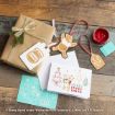 A wooden table with a wrapped gift, a honey pot tag, a bear ornament, a red ink stamp, cards featuring Winnie the Pooh, and envelopes. Some cards say “Merry Everything.”.