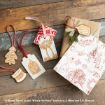 Gift tags and ornaments with Winnie the Pooh Christmas designs are arranged by wrapped presents on a wooden surface. The tags feature gingerbread-style art and festive elements like a Christmas tree and a drum.