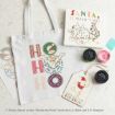 A tote bag with “HO HO HO” and Winnie the Pooh, a Christmas card, two jars of paint, a paintbrush, and a tag reading “Kinda feels like Christmas,” all on a white surface.