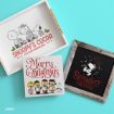 Three Peanuts-themed holiday decorations: a tray with “Snoopy’s Cocoa,” a “Merry Christmas” sign with characters singing, and a framed “Reindeer Crossing” design with Snoopy on a sleigh, on a blue background.
