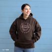 A person in a brown hoodie with “Sip Coffee, Read Books, Gilmore Girls” text and book graphic stands smiling in front of a blue wooden wall.