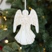 A white and gold angel ornament hangs on a Christmas tree with green needles and glowing string lights in the background.