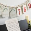 A music sheet on a piano, lit candles, and a holiday garland with numbered tags and handwritten words like “Light the World” and “Redeemer.” Decorative beads hang above, creating a festive atmosphere.