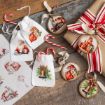 Christmas-themed gift bags, round ornaments with festive designs, candy canes, a wrapped present with red and white ribbon, and a sheet of Christmas stickers on a rustic wooden surface.