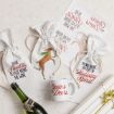 Festive scene with wine bags, a mug, and gift wrap. Bags read “Dear Santa, please bring me wine” and “I’m not drunk, I’m full of holiday spirit.” A bottle, mug, and wrapped gift are nearby.