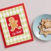 A greeting card with a broken gingerbread figure and the words “Oh Snap!” beside a blue plate holding star-shaped iced gingerbread cookies.