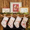 Four Christmas stockings hang from a mantel decorated with a wood bead garland, pine branches, and framed festive art, including Santa Claus and reindeer images.