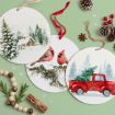 Three round ornaments with winter scenes: a snowy cabin, two cardinals on a branch, and a red truck with a Christmas tree. Surrounded by pinecones, red berries, wooden beads, snowflakes, and cinnamon sticks on a green background.