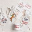Gift bags with reindeer illustrations and holiday phrases, a mug reading “Cheers my Deers,” and festive printed cards laid out on a light surface.