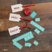 Three decorated name tags with red ribbons read “Noah,” “Emily,” and “Gracie.” Blue letter and number stickers and a small red paint jar are also on a wooden surface.