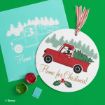 Round Christmas decor shows Mickey Mouse driving a red truck with a tree in the back, and “Home for Christmas!” text below. Green and red paint pots, a blue tool, and a print of the design are nearby on a green surface.
