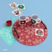 Two mugs with Disney characters, matching coasters, chopsticks, and a red placemat with white snowflakes on a light blue surface. There are also decorative cards, a bowl of red sauce, and aqua-colored paper with snowflake designs.