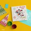 A holiday-themed art kit with a canvas of Mickey and Minnie Mouse sledding, two paint cups (red and green), and festive patterned paper on a yellow background.