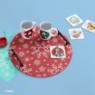 Two Disney mugs and coasters with character designs are on a red snowflake mat. Pens, paper squares, and more coasters featuring Disney characters are spread out on a blue background.