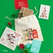 A holiday-themed drawstring bag with Mickey Mouse, surrounded by Christmas cards, ornaments, paint, and gifts, on a green background.