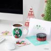 A festive desk setup with a Mickey Mouse mug of hot chocolate, Disney character coasters, a NOEL card, a small Christmas tree, a red jar, and a decorative triangular ornament.