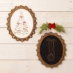 Two oval framed holiday drawings hang on a white wood wall. The left shows a Christmas tree; the right shows a hanging ornament. Greenery with a red bow decorates above the right frame.