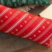 Rectangular red pillow with diagonal white stripes and small white floral patterns, resting on a wooden floor next to a green pillow with tree designs and a beige book.