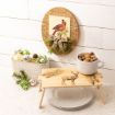 Festive decor with a cardinal sign, a container of ornaments, and a cup of nuts on a wooden tray with a deer design, set on stacked white plates against a white wood wall.