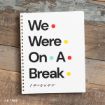 A spiral notebook on a wooden surface with bold text: “We Were On A Break” and colorful dots, referencing the TV show “Friends.”.